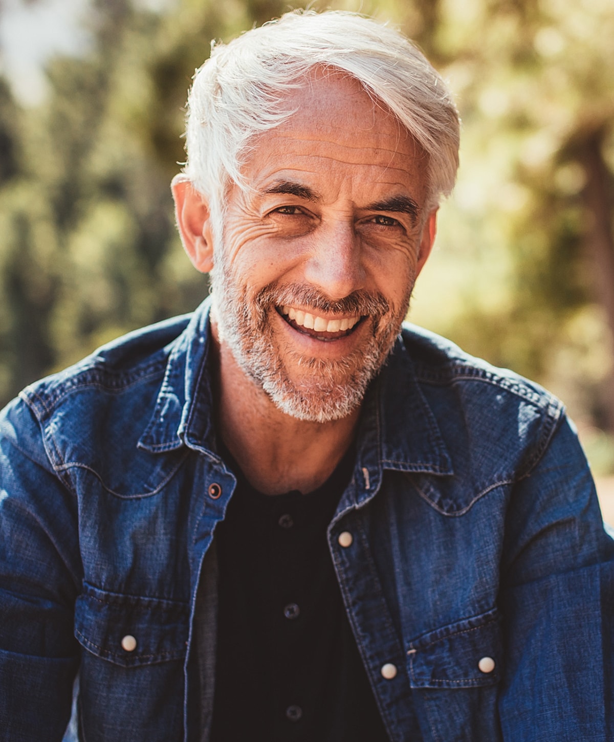Smiling older man in denim jacket outdoors.