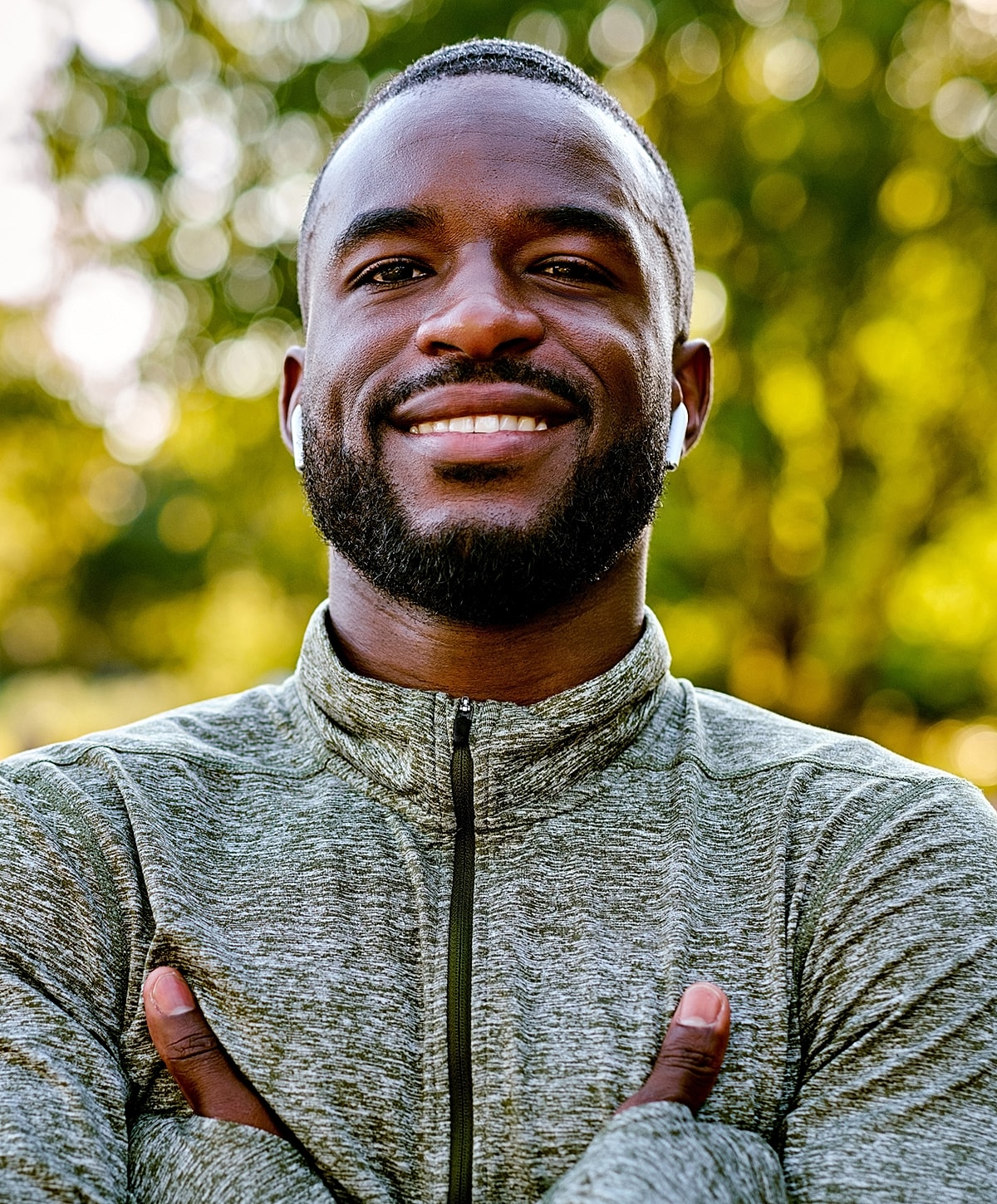 Smiling man outdoors with arms crossed confidently.