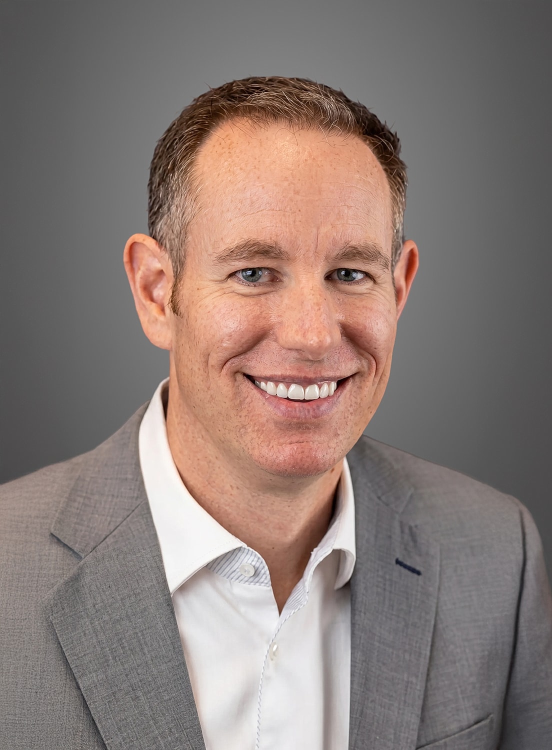 Smiling man in professional attire with gray background.