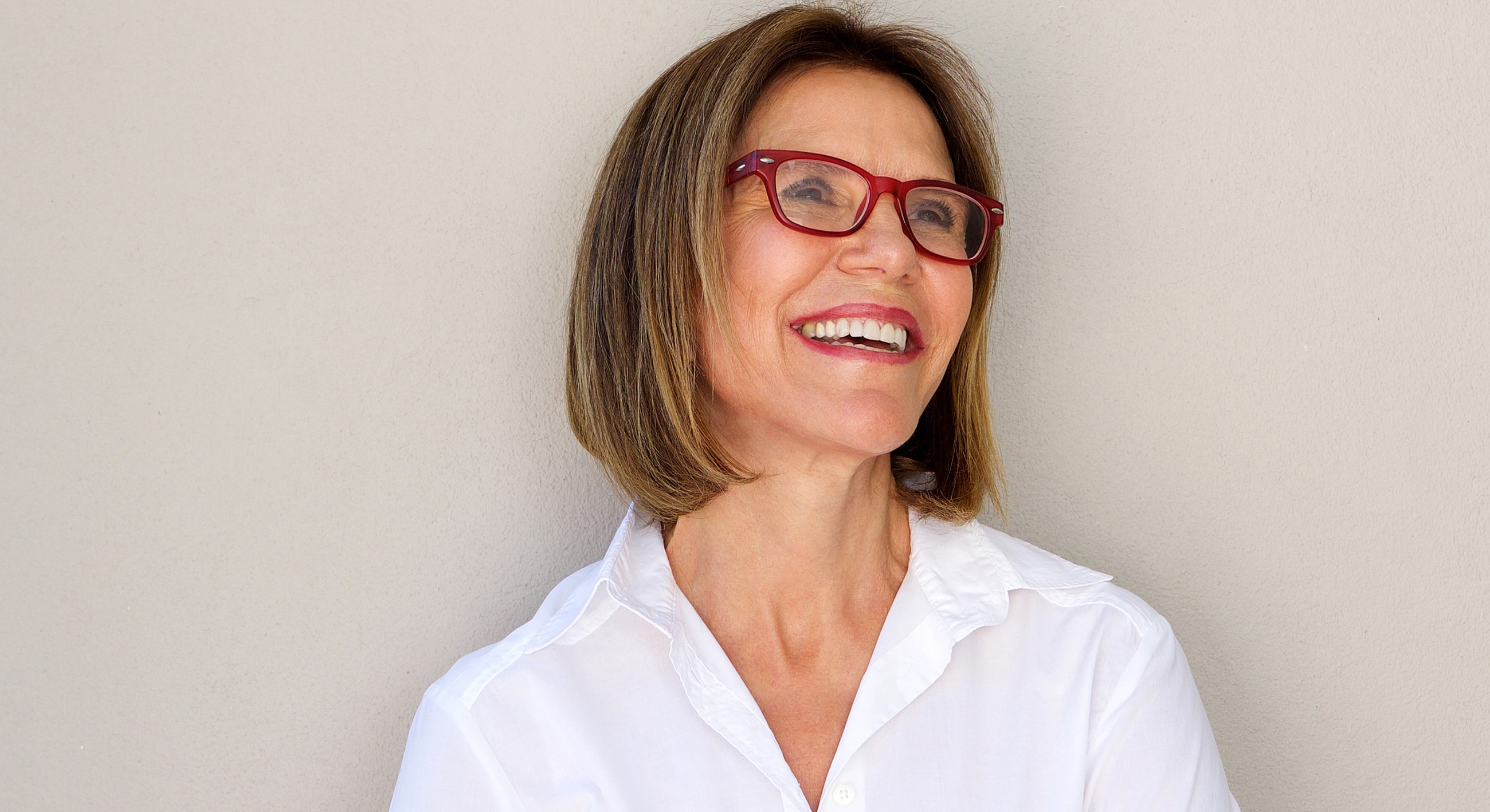 Smiling woman in glasses against neutral background.