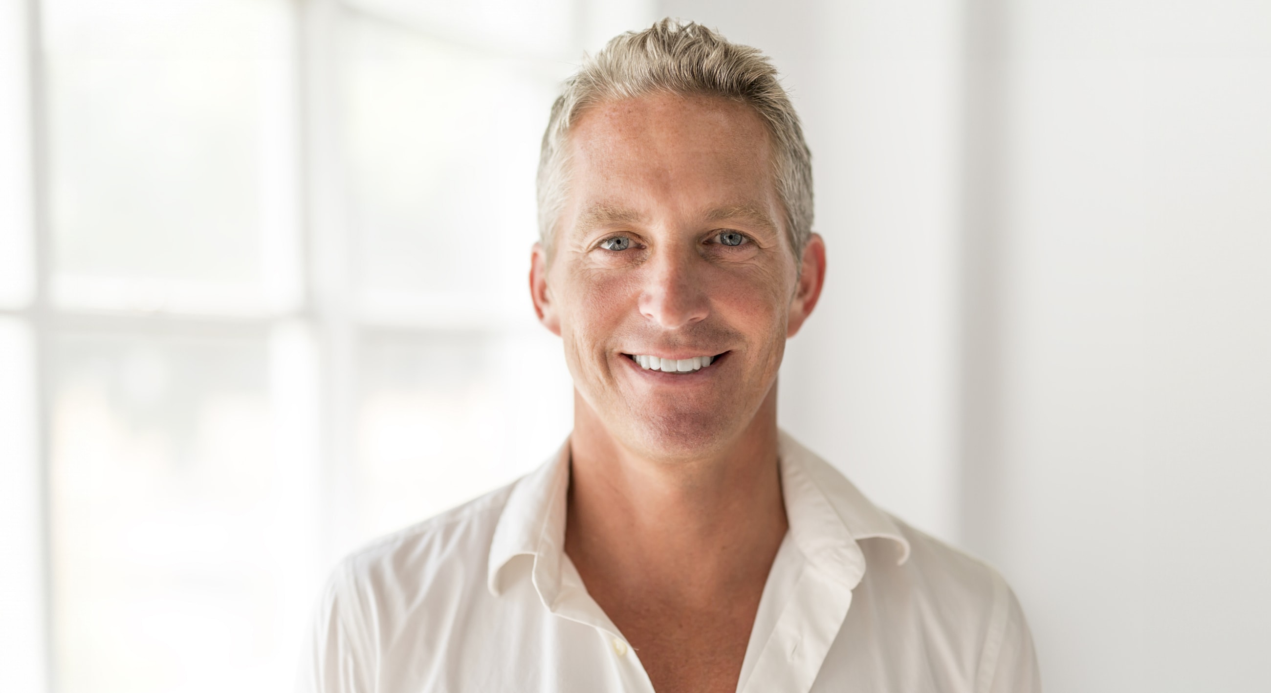 Smiling man in a white shirt, indoor setting.