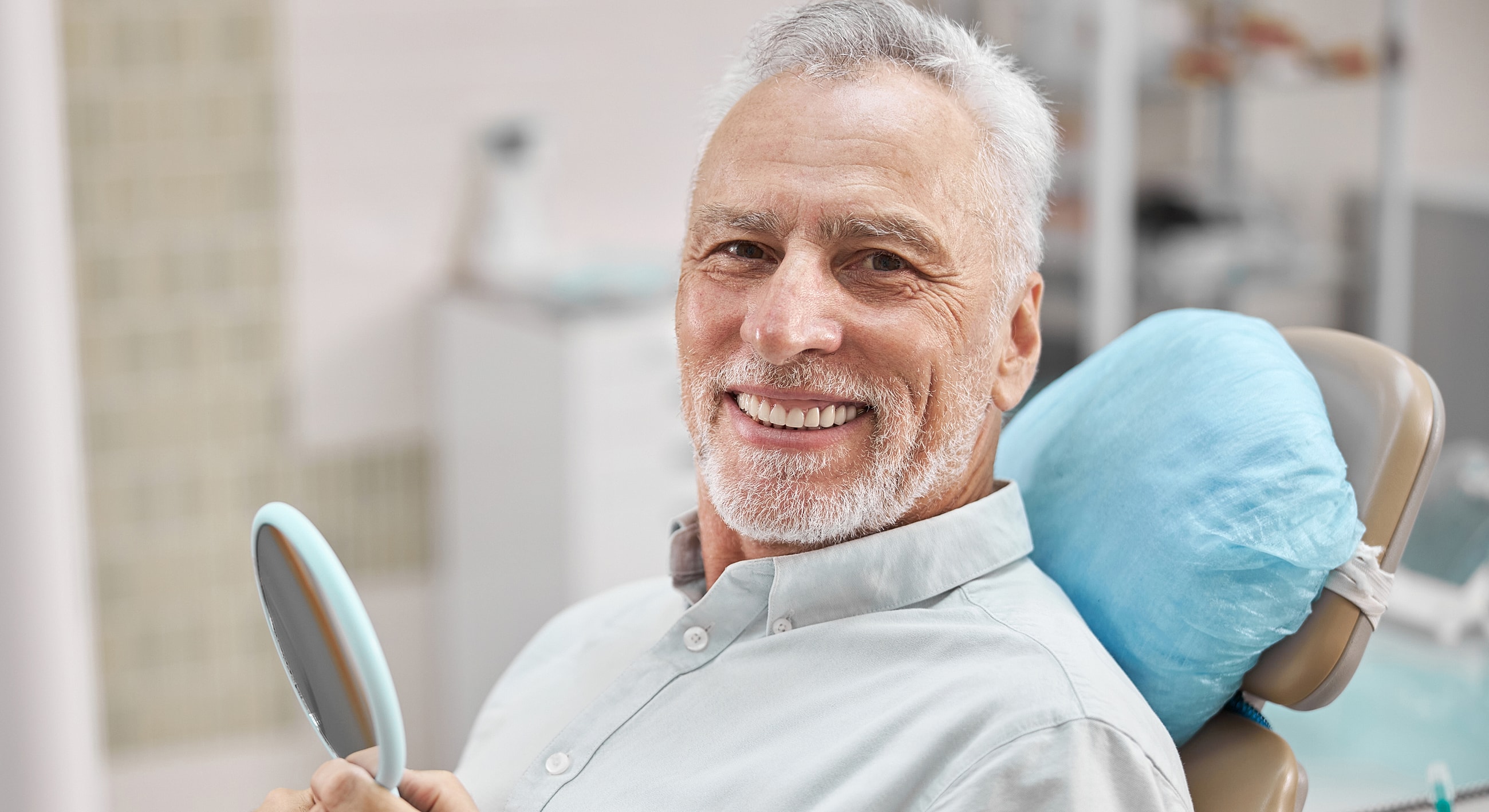 Smiling patient in dental chair holding mirror